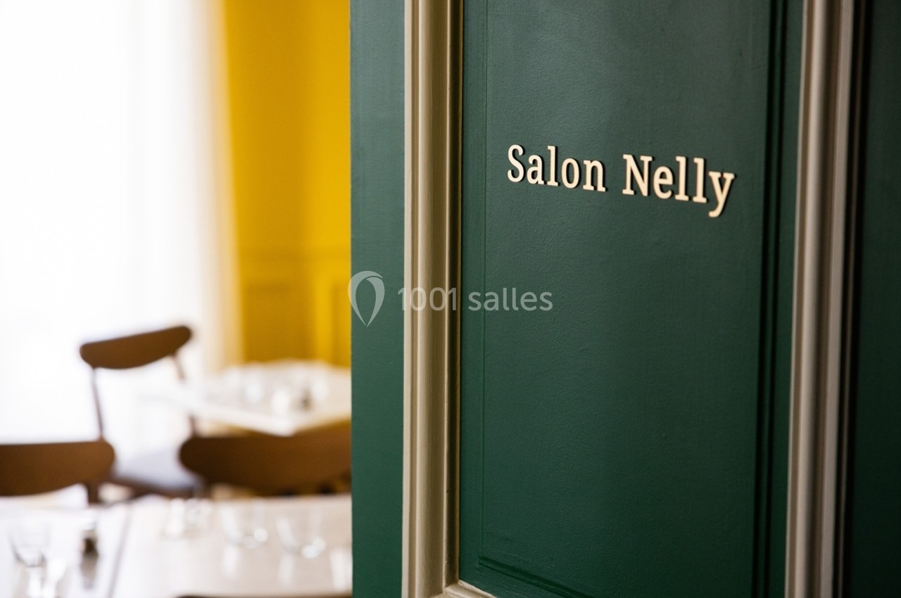 Porte verte avec l'inscription ’Salon Nelly’, donnant sur une salle lumineuse avec des tables et des chaises en bois.