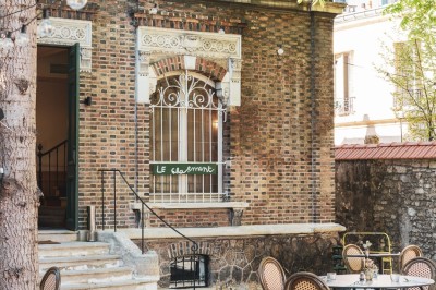 Cour extérieure avec tables et chaises en rotin, décorée de guirlandes colorées, devant une maison en briques.