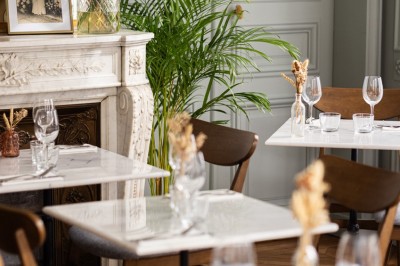 Cour extérieure avec tables et chaises en rotin, décorée de guirlandes colorées, devant une maison en briques.