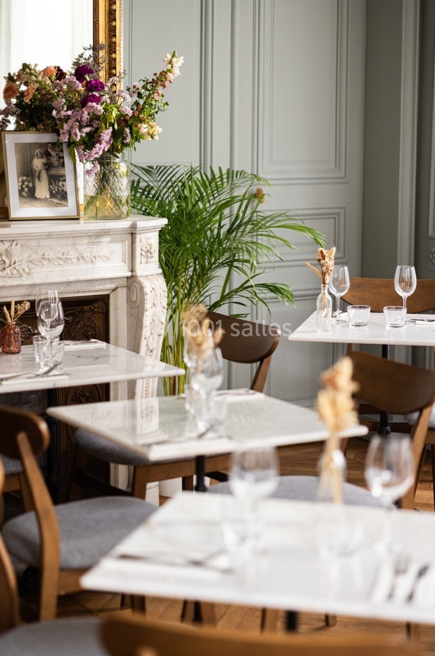 Salle de restaurant élégante avec tables en marbre, chaises en bois, fleurs séchées et cheminée décorée de fleurs.