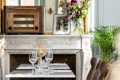Cour extérieure avec tables et chaises en rotin, décorée de guirlandes colorées, devant une maison en briques.