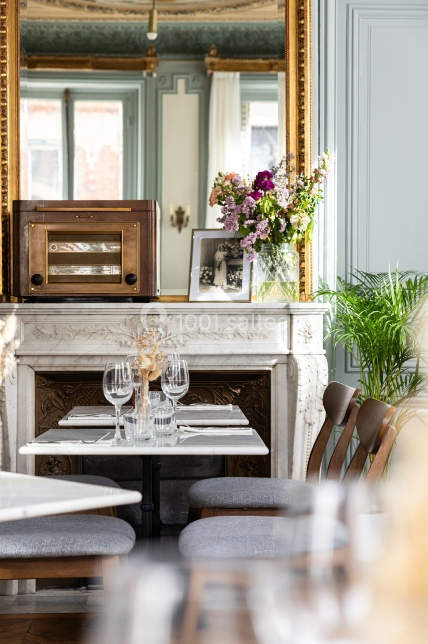 Table dressée devant une cheminée en marbre ornée d'un miroir doré, avec un bouquet de fleurs et une radio vintage.