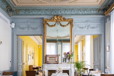 Cour extérieure avec tables et chaises en rotin, décorée de guirlandes colorées, devant une maison en briques.