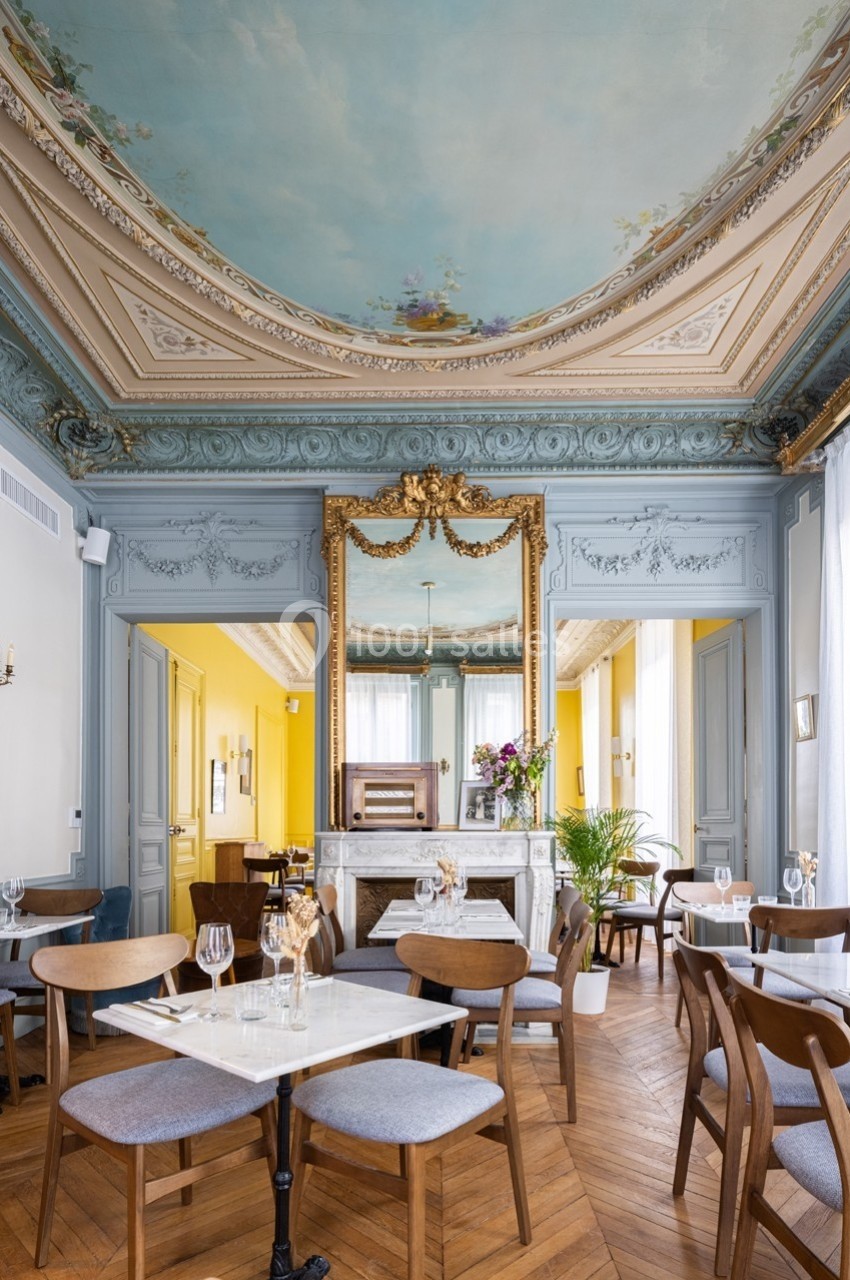 Salle de restaurant élégante avec plafond peint, moulures, miroirs dorés, tables dressées et parquet en bois.