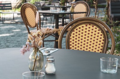 Cour extérieure avec tables et chaises en rotin, décorée de guirlandes colorées, devant une maison en briques.