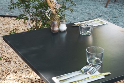 Cour extérieure avec tables et chaises en rotin, décorée de guirlandes colorées, devant une maison en briques.