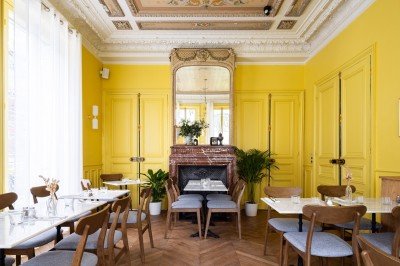 Cour extérieure avec tables et chaises en rotin, décorée de guirlandes colorées, devant une maison en briques.