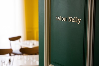 Cour extérieure avec tables et chaises en rotin, décorée de guirlandes colorées, devant une maison en briques.
