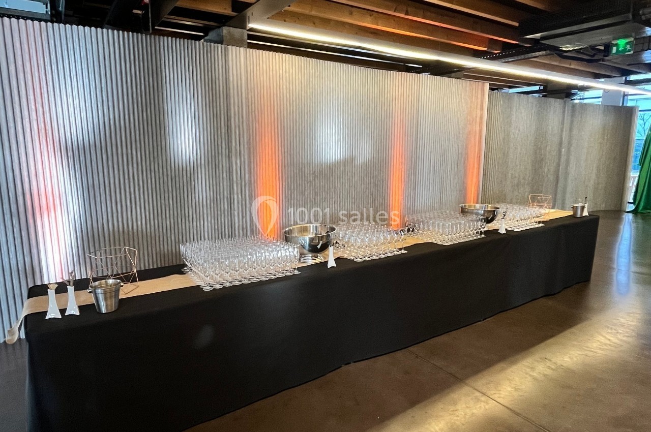 Table dressée avec une nappe noire, alignée de verres et seaux à champagne, éclairée par des lumières orange.