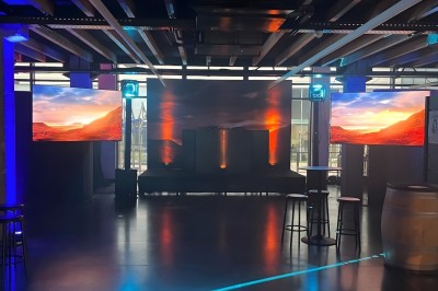 Salle sombre avec deux écrans affichant un paysage désertique, éclairages colorés et mobilier minimaliste.