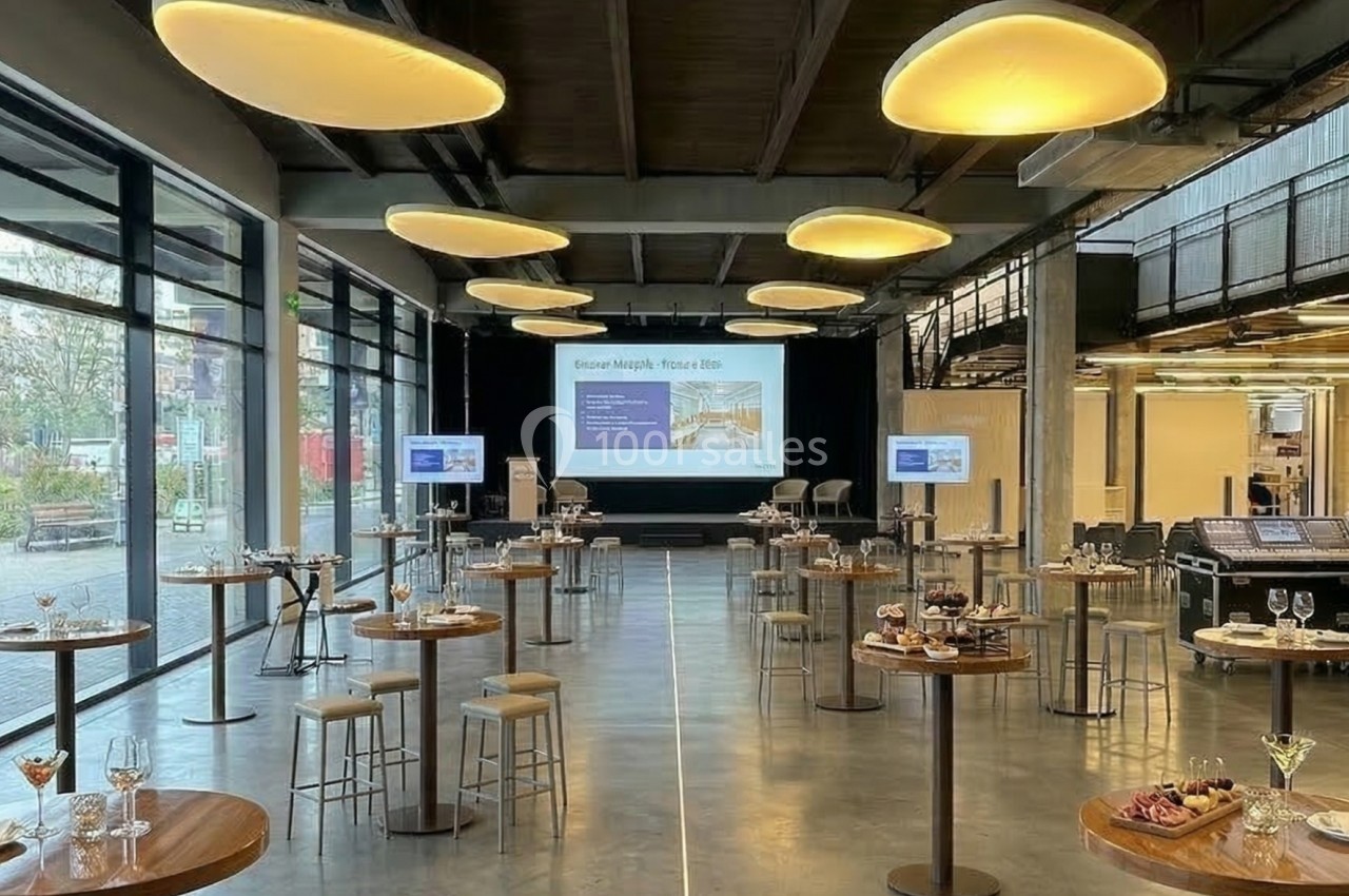 Salle de conférence moderne avec tables hautes, écrans de présentation et éclairage suspendu.