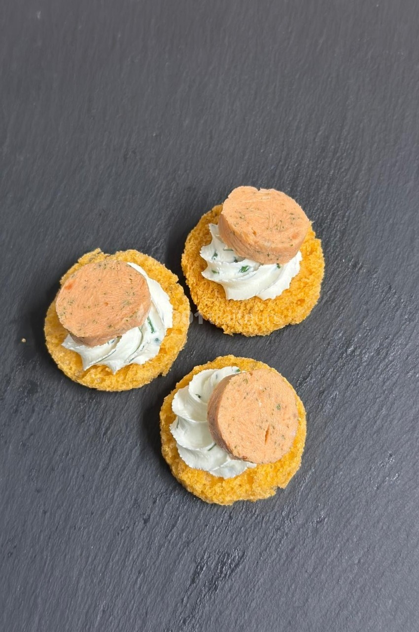 Trois canapés sur ardoise, composés de crackers, crème blanche aux herbes et rondelles de garniture saumonée.