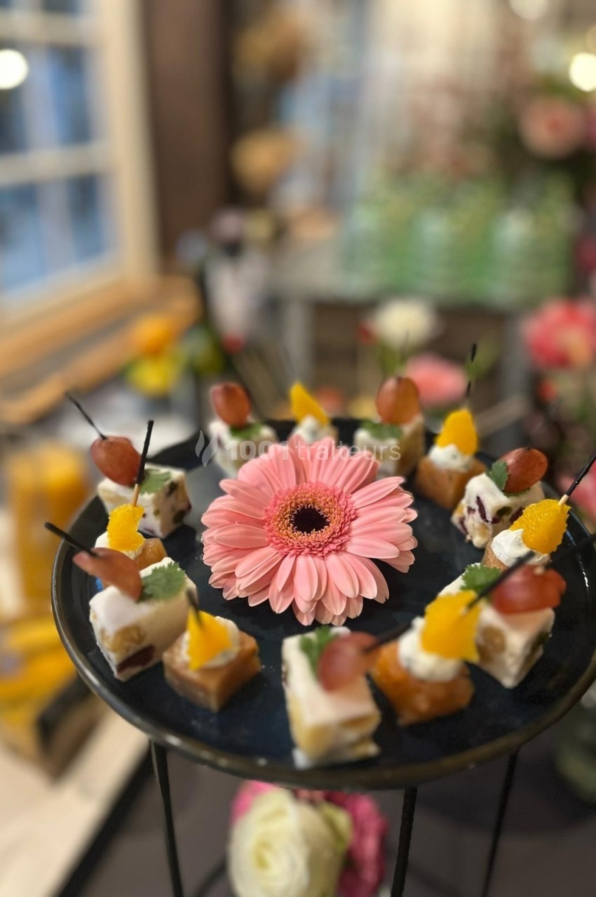 Plateau de bouchées apéritives décoré d'une fleur rose au centre, disposé sur un support noir.