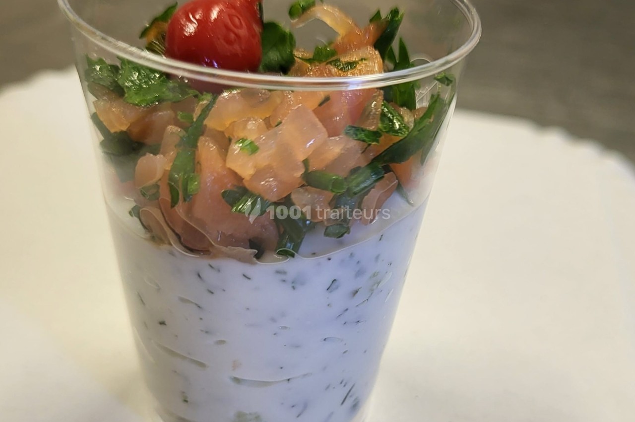 Verrine composée de crème aux herbes, dés de saumon fumé, persil frais et une petite tomate cerise rouge.