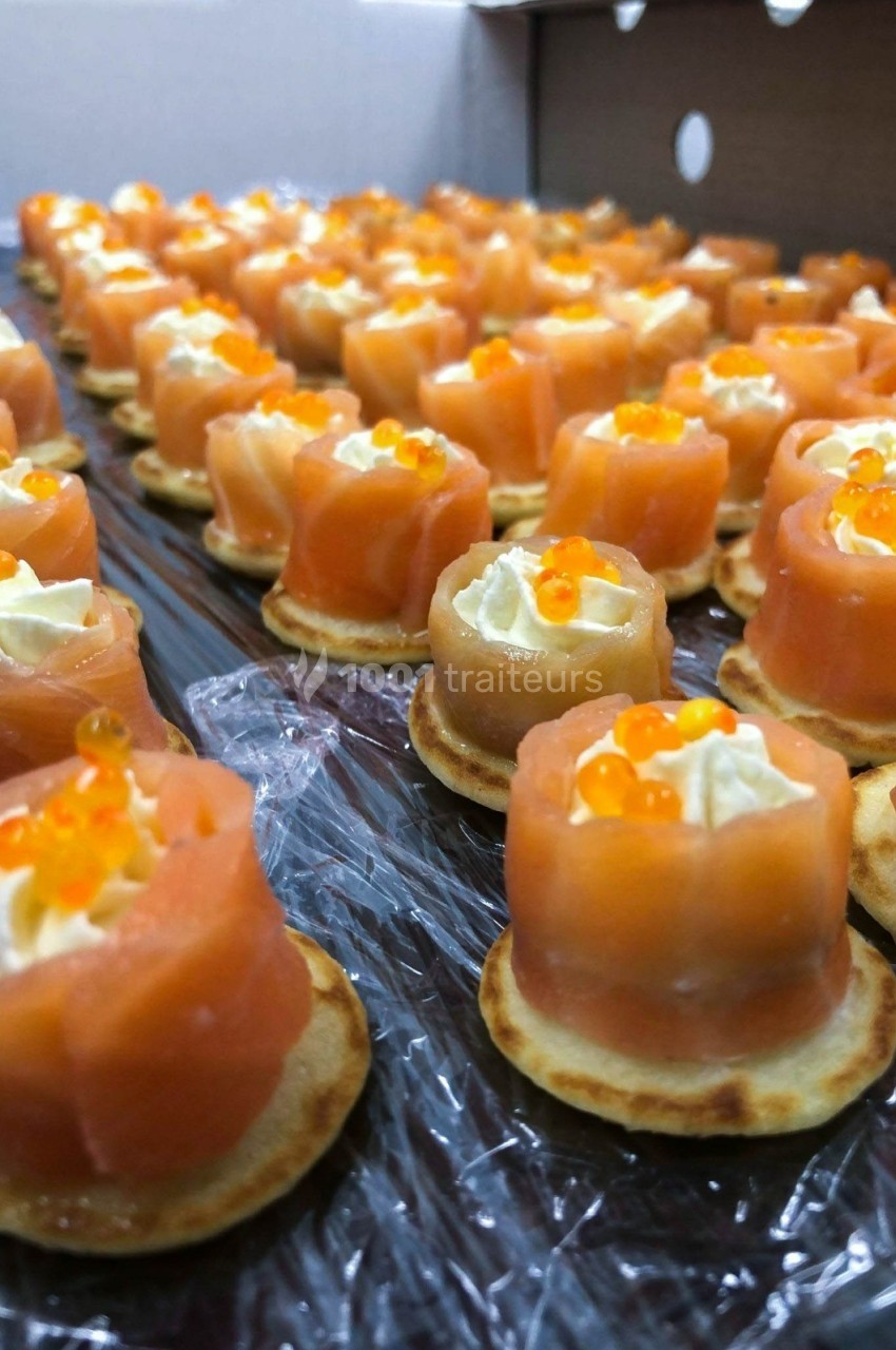 Bouchées apéritives au saumon fumé, crème et œufs de poisson sur mini-blinis disposés en rangées.