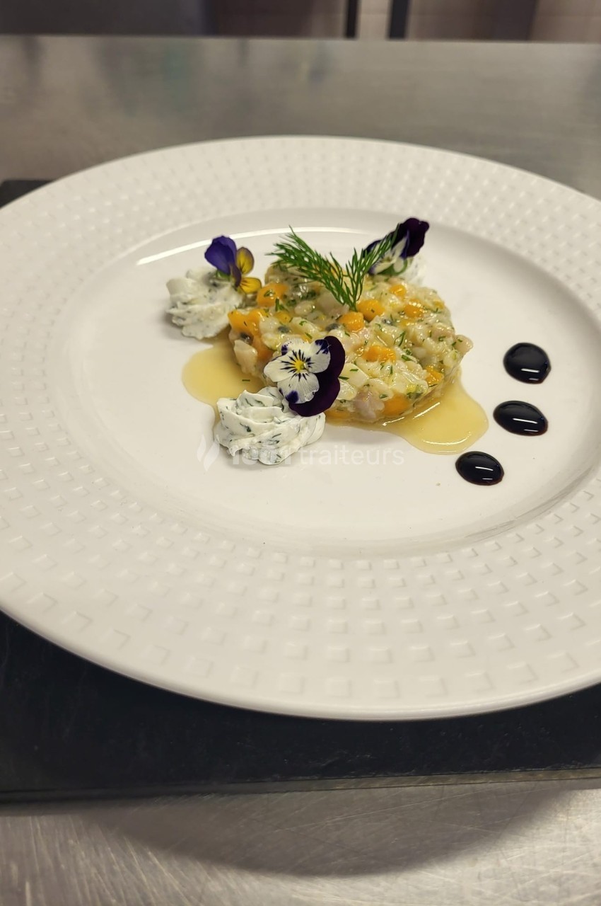 Assiette de tartare de poisson décorée de fleurs comestibles, herbes fraîches et sauces artistiquement disposées.