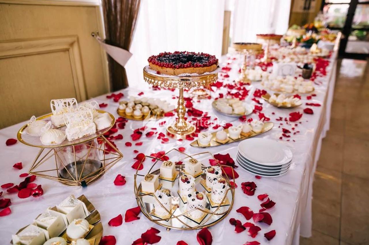 Table décorée avec des pétales de roses rouges, garnie de desserts variés et d'une tarte aux fruits sur un présentoir doré.