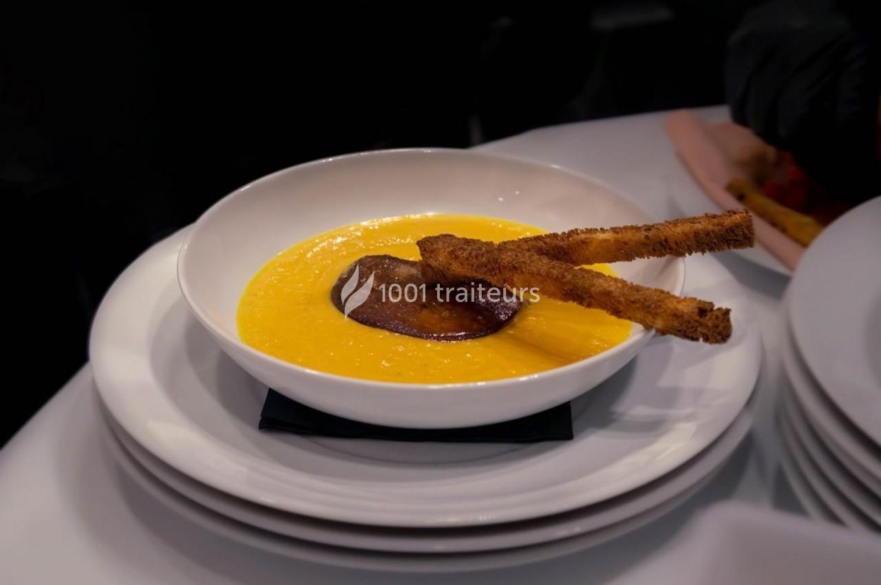 Bol de soupe orange garnie d'une tranche de légume grillé et de deux bâtonnets croustillants.