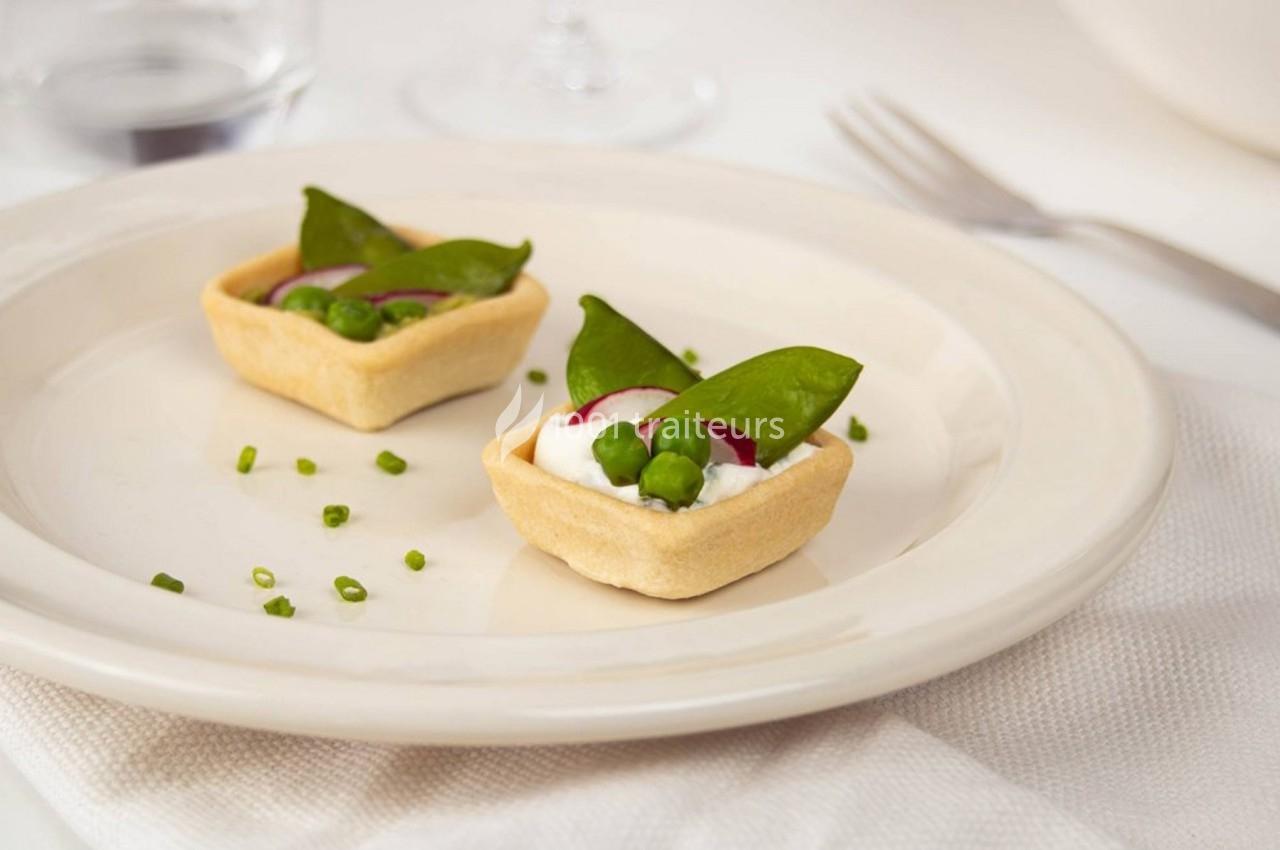 Deux bouchées apéritives dans des tartelettes garnies de fromage, petits pois, radis et feuilles vertes sur une assiette…