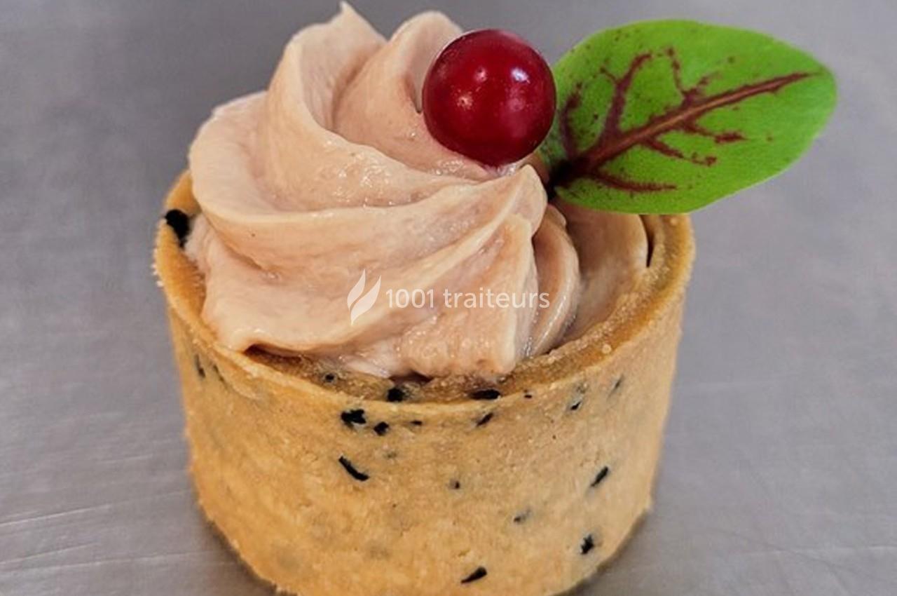 Tartelette garnie d'une mousse beige, décorée d'une feuille verte et d'une baie rouge sur un fond gris.