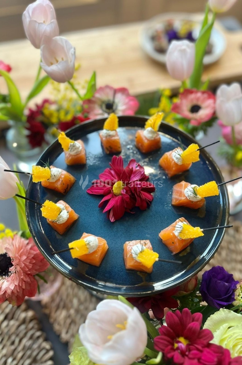 Plateau de bouchées de saumon avec décoration florale colorée en arrière-plan.