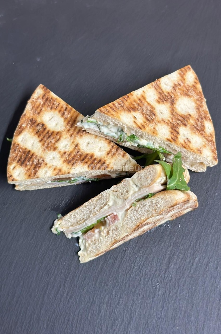 Triangles de sandwich grillé garnis de roquette, fromage et jambon, présentés sur une surface noire.