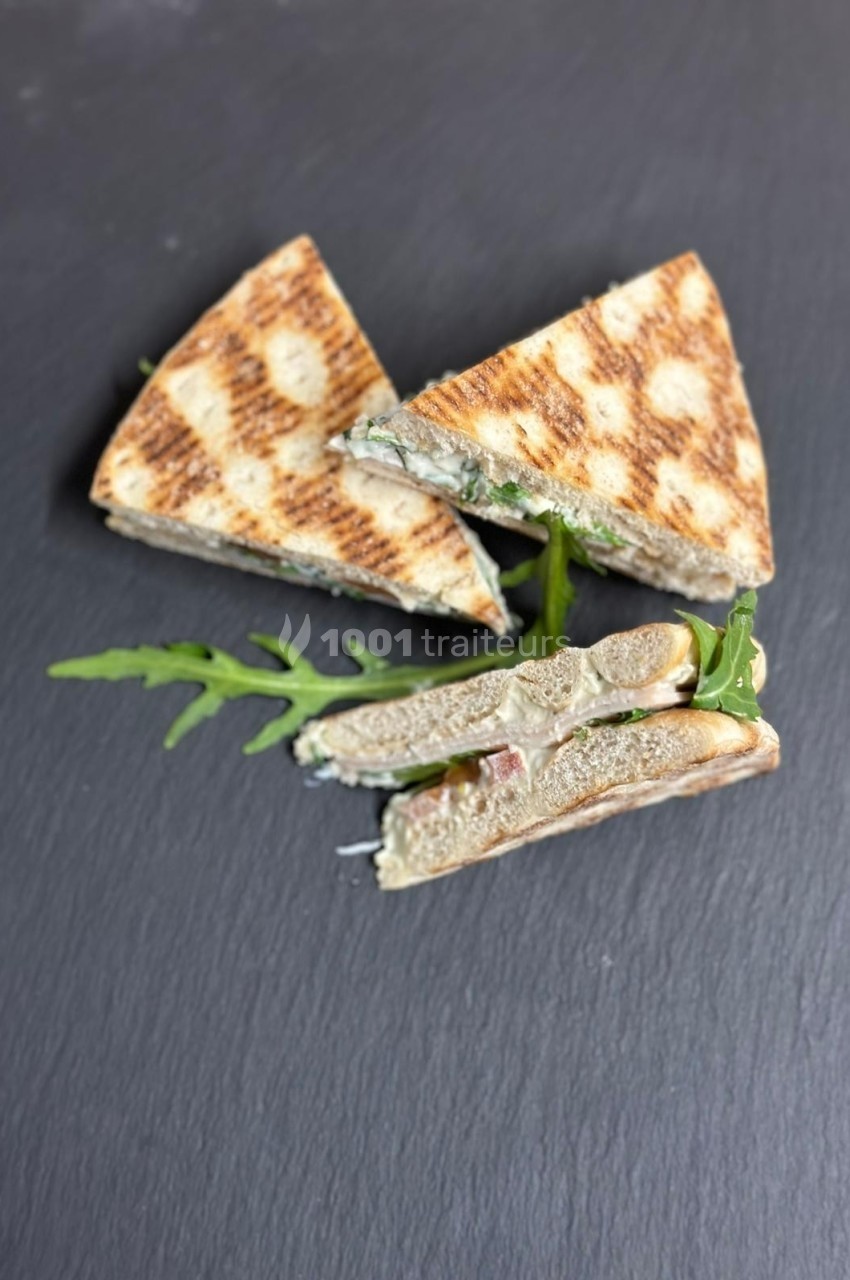 Triangles de sandwichs grillés garnis de roquette et d'une farce crémeuse, présentés sur une ardoise noire.