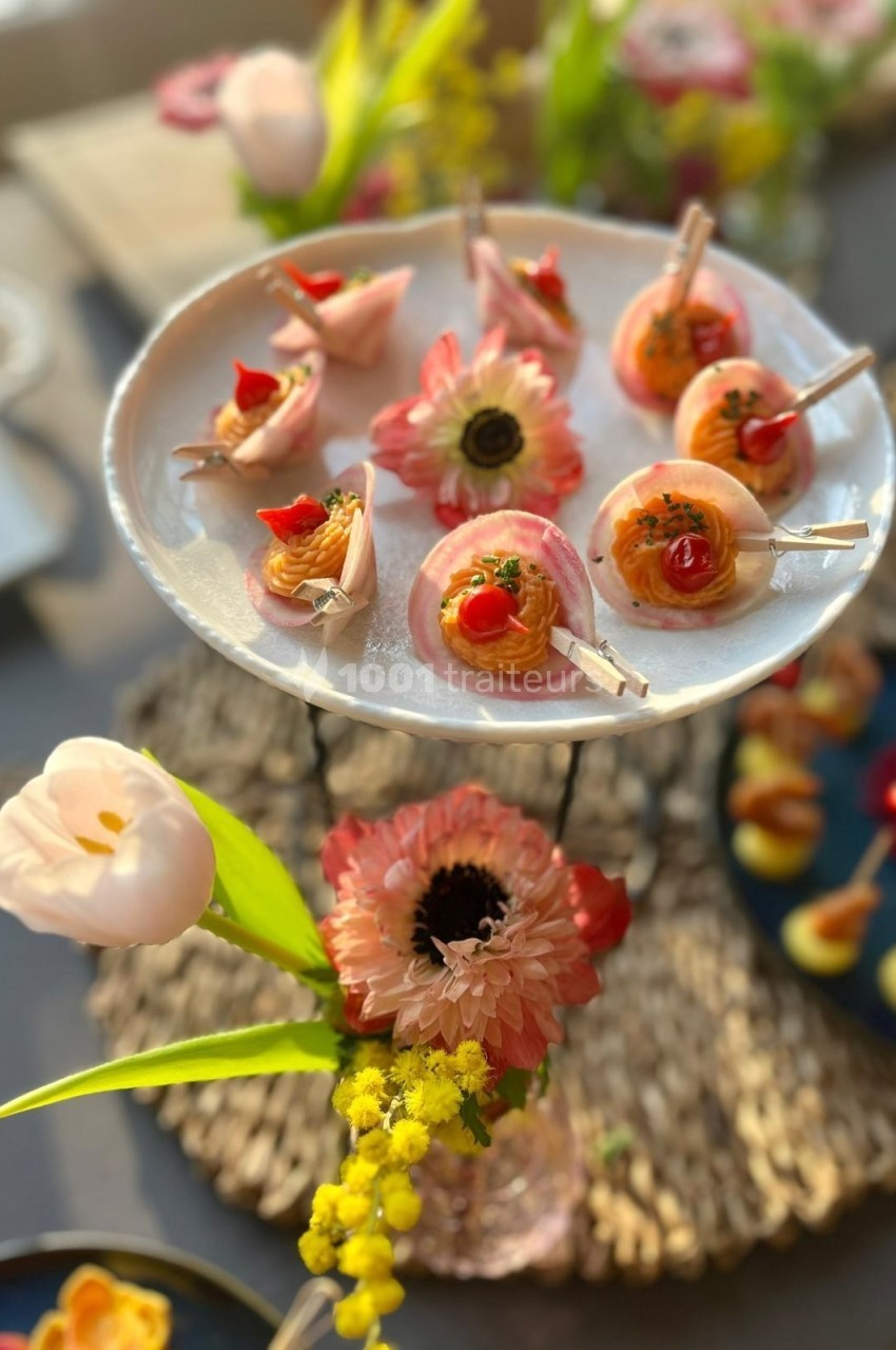 Plateau de bouchées apéritives colorées sur un présentoir, entouré de fleurs décoratives.