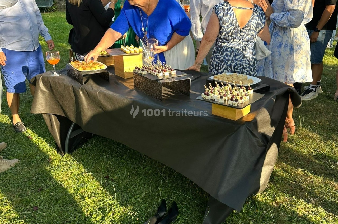 Personnes se servant de petits amuse-bouches sur une table recouverte d'une nappe noire lors d'un événement en plein air.