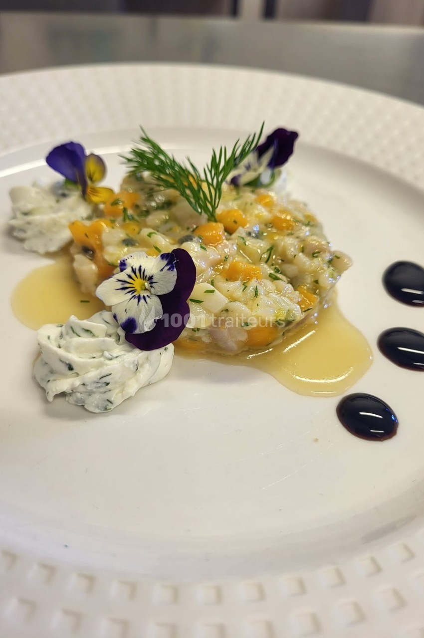 Assiette de tartare de poisson décorée de fleurs comestibles, crème aux herbes et traits de sauce balsamique.