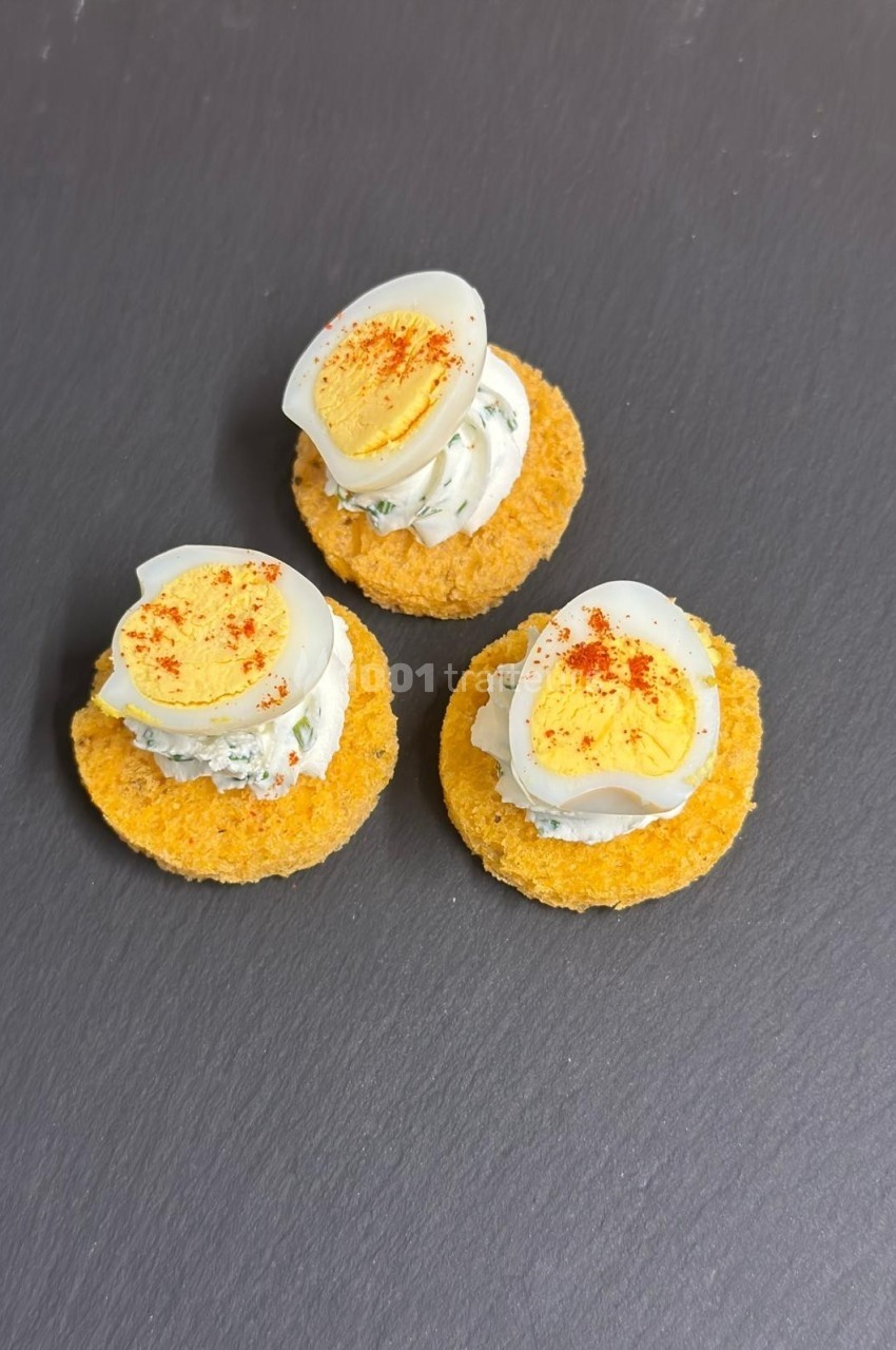 Trio de canapés sur une ardoise, garnis de crème, demi-œufs durs et une pincée de paprika.