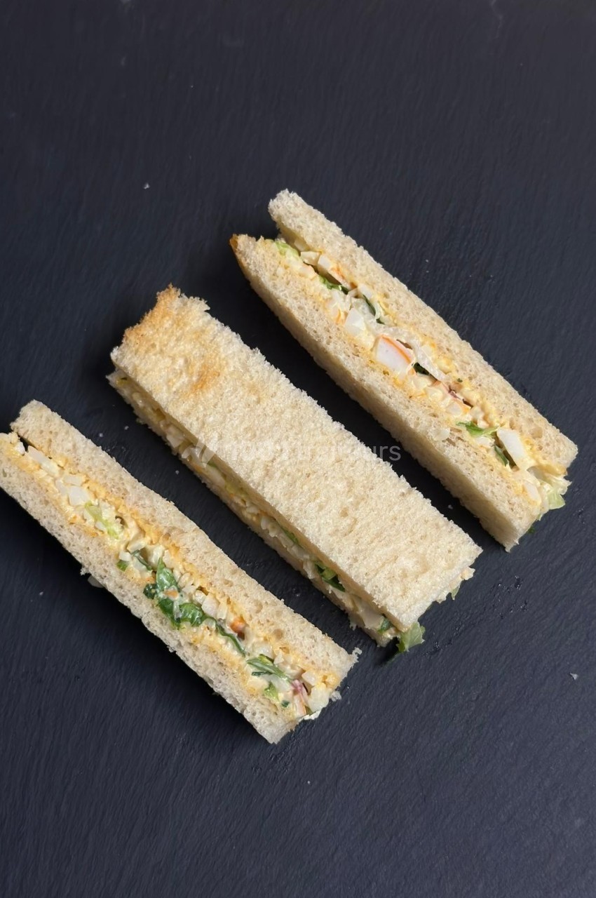 Trois sandwichs triangulaires garnis de légumes et d'œufs, présentés sur une surface noire.