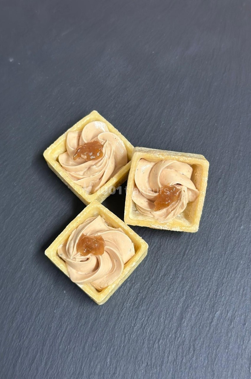 Tartelettes carrées garnies de crème et décorées d'une touche de caramel, posées sur une surface ardoisée.
