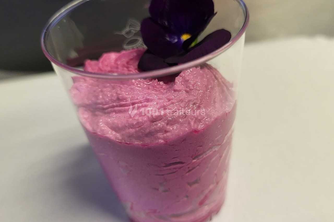 Mousse rose servie dans un verre transparent, décorée d'une fleur violette comestible.
