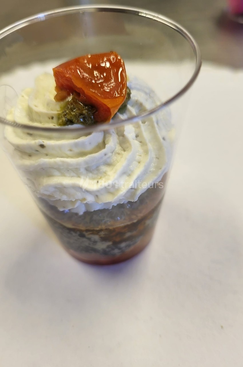 Verrine garnie de couches de crème, tapenade et tomate confite sur un fond blanc.