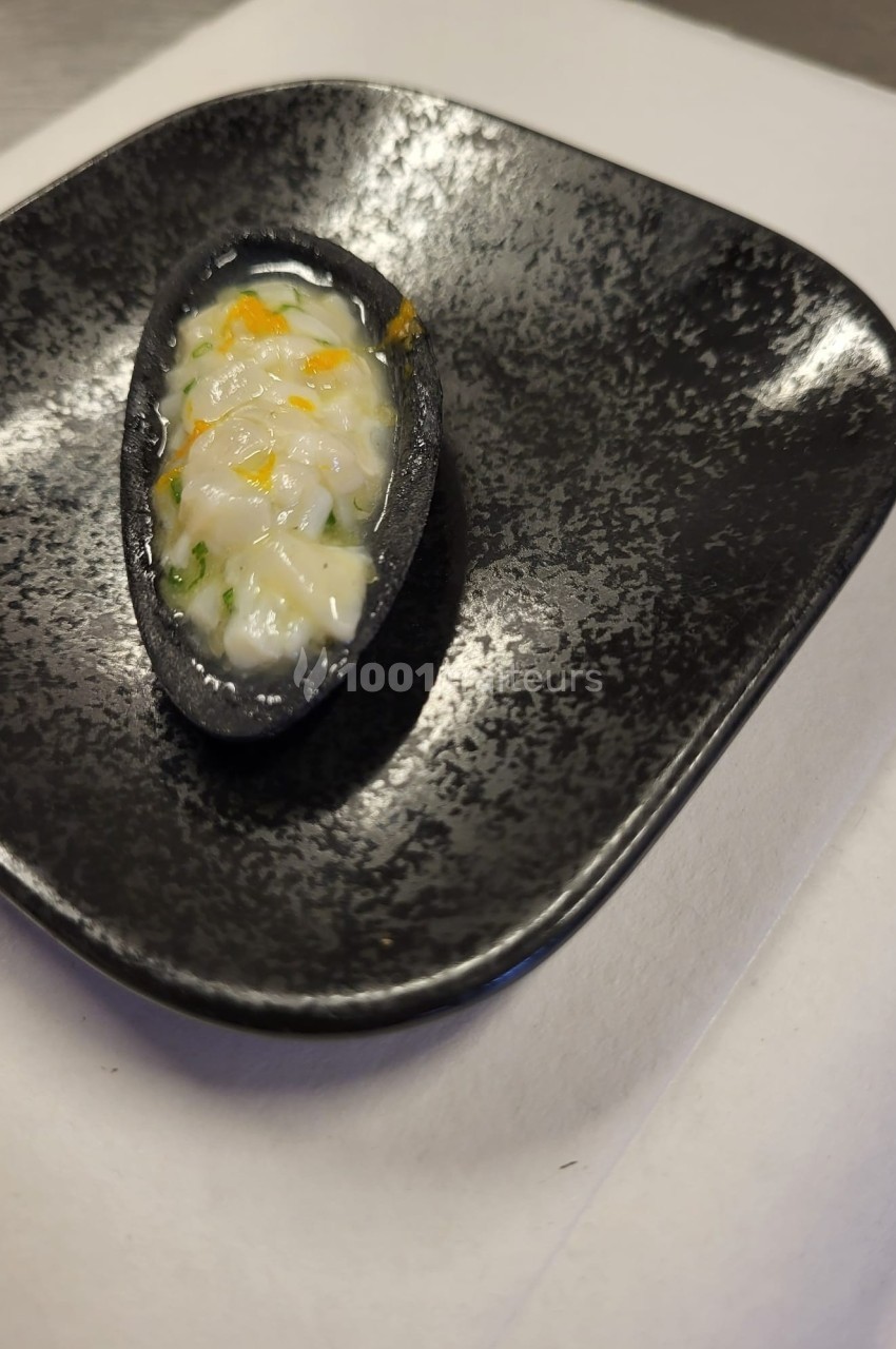 Une bouchée servie dans une coque noire, garnie de préparation crémeuse avec des touches de jaune et vert.