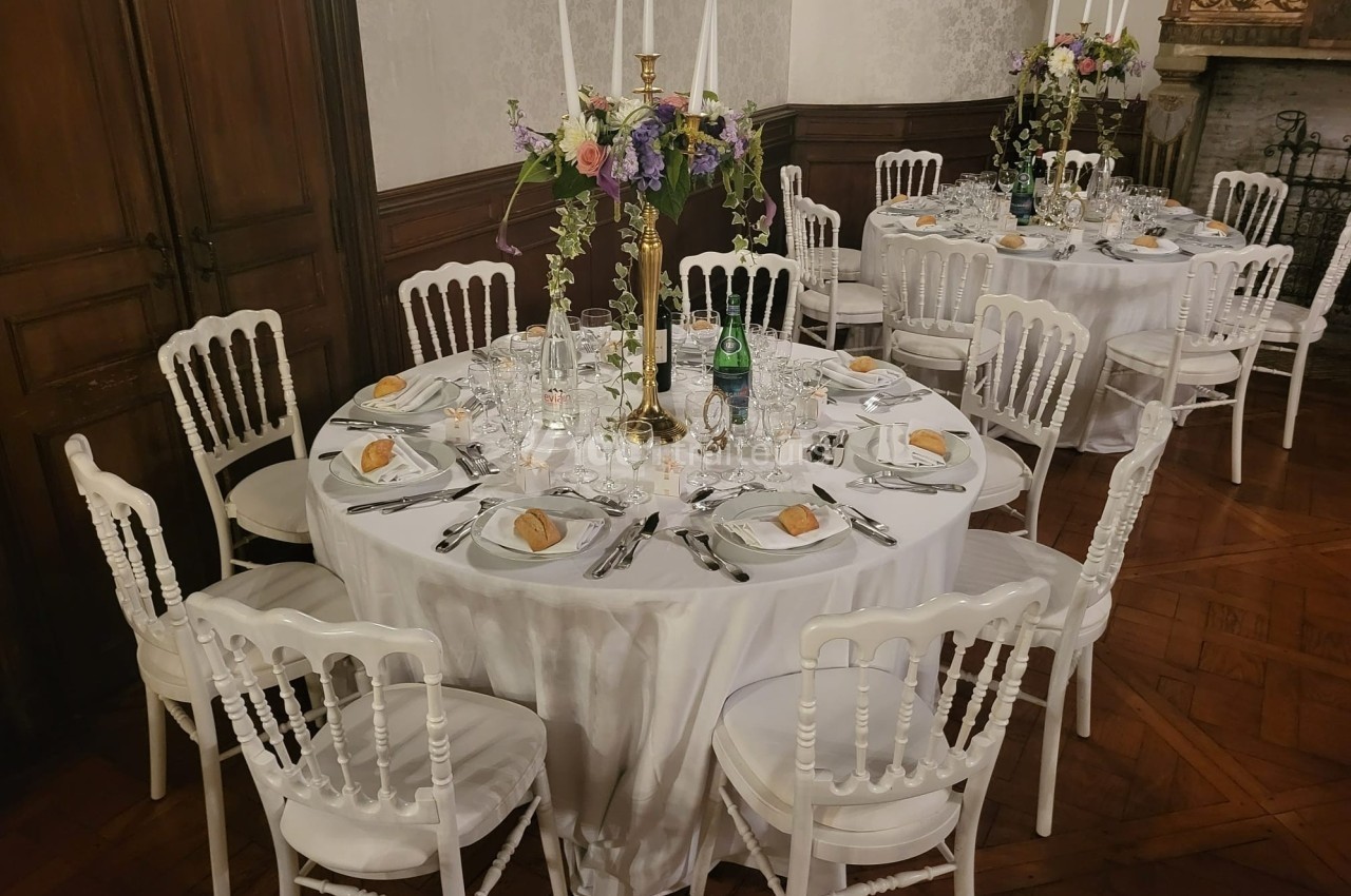 Tables rondes élégamment dressées avec nappes blanches, chaises assorties et centres de table floraux dans une salle…
