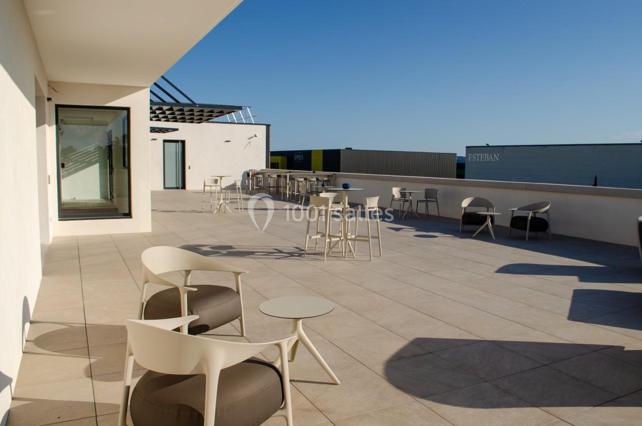 Terrasse spacieuse avec mobilier moderne, tables et chaises, offrant une vue dégagée sous un ciel bleu.