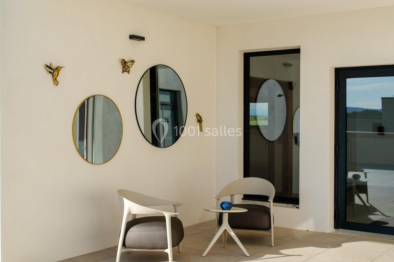Deux fauteuils modernes et une table basse sur une terrasse lumineuse avec des miroirs et des décorations murales.