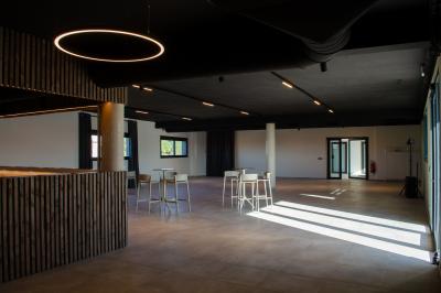 Salle spacieuse avec sol carrelé, éclairage moderne, grandes fenêtres et quelques tables hautes dispersées.