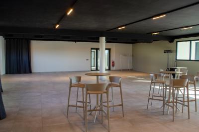 Salle spacieuse avec sol carrelé, éclairage moderne, grandes fenêtres et quelques tables hautes dispersées.