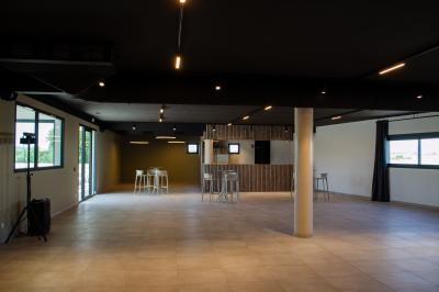 Salle vide avec sol en carrelage, murs clairs, plafond sombre, grandes fenêtres et quelques tables hautes avec tabourets.