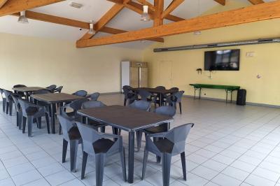 Salle lumineuse avec charpente en bois apparente, tables et chaises disposées sur un sol carrelé blanc.