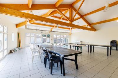 Salle lumineuse avec charpente en bois apparente, tables et chaises disposées sur un sol carrelé blanc.