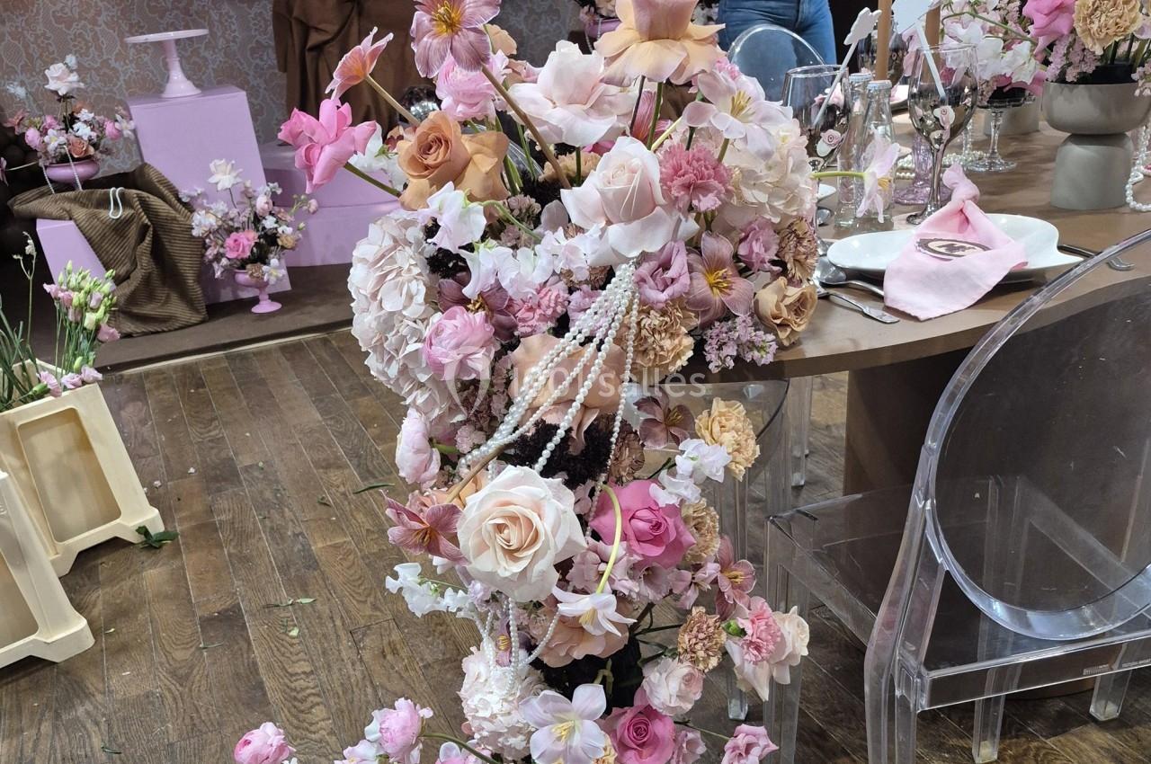 Arrangement floral rose et blanc avec des perles, posé sur un sol en bois dans un décor de fête élégante.