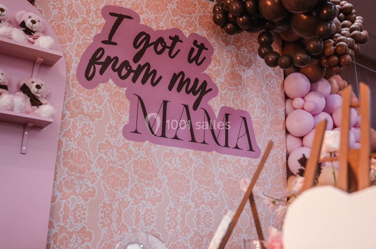 Mur décoratif avec inscription ’I got it from my mama’, ballons roses et marron, et étagère avec peluches.