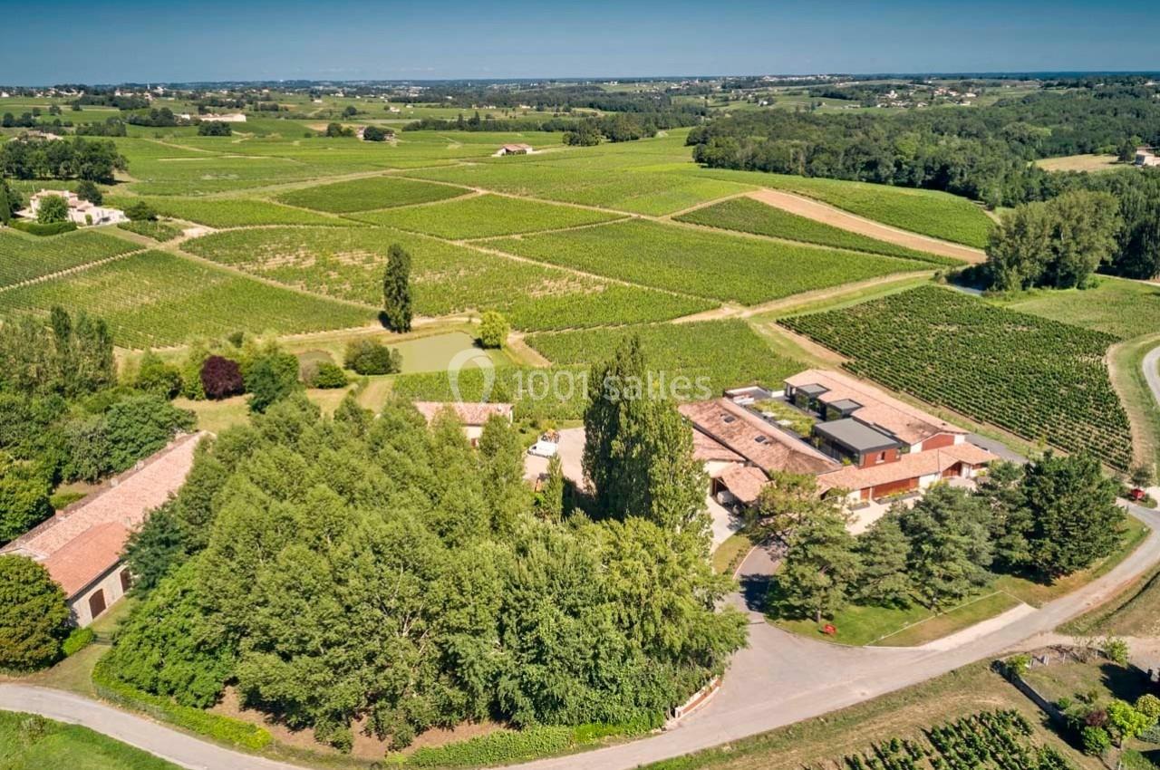 Vue aérienne d'un domaine entouré de vignobles et de verdure sous un ciel dégagé.
