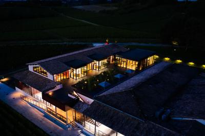 Bâtiment moderne avec façades vitrées et terrasses en bois, entouré de végétation au crépuscule.