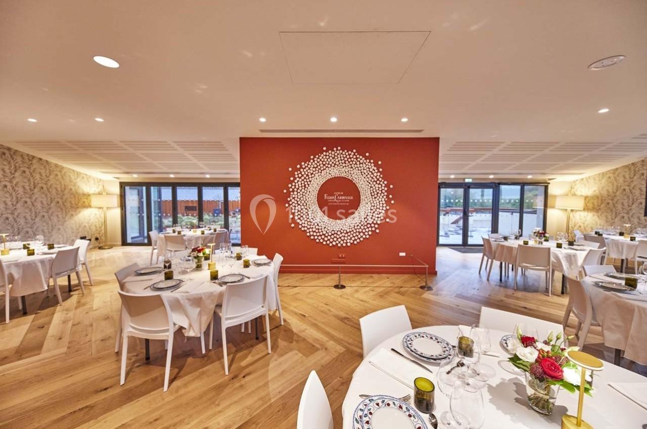 Salle de réception lumineuse avec tables dressées, décorée d'un mur rouge orné d'un motif circulaire blanc.