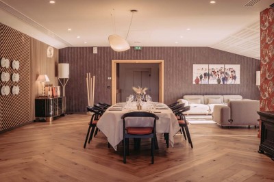 Bâtiment moderne avec façades vitrées et terrasses en bois, entouré de végétation au crépuscule.